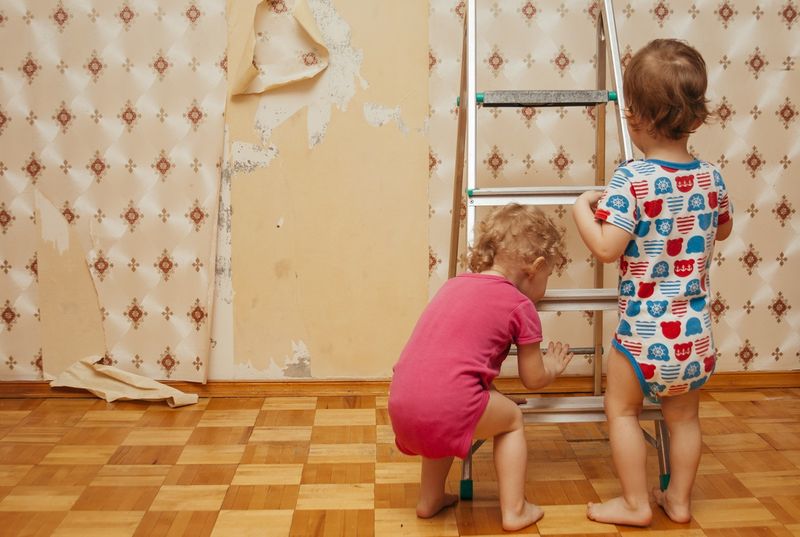 Два ребенка в пижамах отдирают обои от стены.